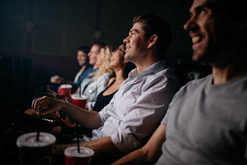 Group of young people sitting in cinema hall watching movie. Multiracial group of friends watching movie in theater.